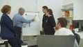 Tired man works at the laptop, workmates dehind himlooks at scheme of apartement on desk