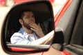 Tired man yawning in auto, view through car side mirror