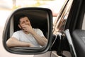 Tired man yawning in auto, view through car side mirror