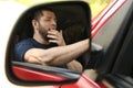 Tired man yawning in auto, view through car side mirror