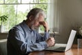 Tired mature 60s man working at laptop from home