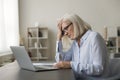 Tired mature senior business woman touching head at laptop Royalty Free Stock Photo