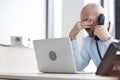 Tired mid adult businessman using telephone at desk in office Royalty Free Stock Photo