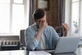 Tired millennial businessman sitting at laptop, rubbing eye lids