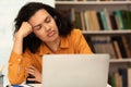 Tired mixed race female student sleeping on table in front of laptop computer, preparing for exams in library Royalty Free Stock Photo