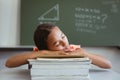 Tired mixed race schoolgirl in classroom sitting at desk sleeping on stack of books Royalty Free Stock Photo