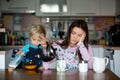 Tired mother, woman drinking coffee in the morning, while child eating breakfast