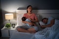 tired mother yawning and breastfeeding newborm baby while her husband sleeping on bed at night Royalty Free Stock Photo