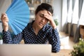 Tired overheated indian woman waving fan suffer from heat indoors