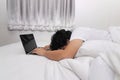 Tired overworked young Asian man with laptop sleeping on the white bed in bedroom. Work from home and quarantine concept Royalty Free Stock Photo