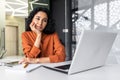 A tired and pensive young woman sits in the office at the table and looks at the laptop screen, resting her head Royalty Free Stock Photo