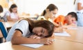 Tired preteen schoolgirl sleeping at desk in classroom during lesson Royalty Free Stock Photo