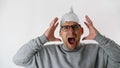 Man in a foil hat in horror screams loudly and holds his hands behind his head. Protective tinfoil helmet to the brain.