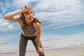 Tired female runner in headphones sweating after cardio exercise and rest after finish on beach Royalty Free Stock Photo