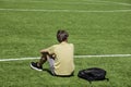 Tired sad alone teenage boy with backpack sitting in empty sport stadium outdoors. Back view