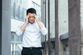 Tired and sad Asian has a severe headache, a businessman outside the office, holding hands behind his head Royalty Free Stock Photo