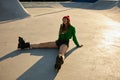 Tired but satisfied teenager girl in roller skates sitting on asphalt rollerdrom
