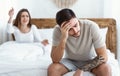 Tired of scandals. Young woman swears, sad man holds his head with hand and sits on bed Royalty Free Stock Photo