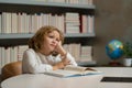 Tired school boy, bored pupil at school. Pupil reading books in a school library. School child doing homework, study Royalty Free Stock Photo