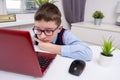 A tired school boy sitting by the table with a laptop and doing homework, e-learning, online education and home school concept Royalty Free Stock Photo