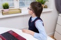 A tired school boy sitting by the table with a laptop and looking through the window while doing homework, e-learning, online Royalty Free Stock Photo