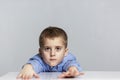 A tired schoolboy boy sits at the table with his arms outstretched forward. Loneliness and learning difficulties. Gray background Royalty Free Stock Photo