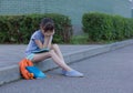 Schoolgirl with a headache sits on the ground. The girl holds on to her head