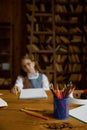 Tired schoolgirl studying at home, selective focus on stationery glass