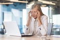 Tired senior gray-haired businesswoman sitting at the desk in the office and holding her head with her hands, feeling Royalty Free Stock Photo