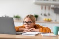 Tired serious pretty european teenage girl pupil in glasses looks at laptop, sits at table Royalty Free Stock Photo