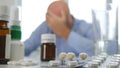 Tired and Sick Person with Medical Pills on the Table Keeping his Head With Hand