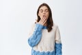 Tired and sleepy girl yawning with closed eyes and opened mouth, feeling bored, standing in sweater against white Royalty Free Stock Photo