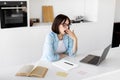 Tired sleepy lady yawning while working or studying on laptop online from home, sitting in modern kitchen, free space Royalty Free Stock Photo