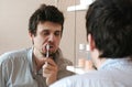 Tired sleepy man with a hangover who has just woken up brush his teeth, looks at his reflection in the mirror. Royalty Free Stock Photo