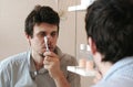 Tired sleepy man with a hangover who has just woken up brush his teeth, looks at his reflection in the mirror. Royalty Free Stock Photo