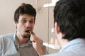 Tired sleepy man with a hangover who has just woken up brush his teeth, looks at his reflection in the mirror. Royalty Free Stock Photo
