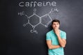 Tired sleepy man yawning over blackboard with drawn caffeine molecule