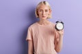 Tired sleepy serious woman holding alarm clock isolated over violet background Royalty Free Stock Photo