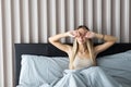 Tired sleepy young woman waking up and yawning with a stretch while sitting in bed Royalty Free Stock Photo