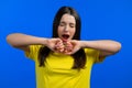 Tired sleepy woman yawns. Girl stretches hands up. Very boring, uninteresting. Blue studio background.