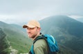 Tired smiling backpacker man in baseball cap walking by the foggy cloudy weather mountain range path with backpack. Active sports Royalty Free Stock Photo