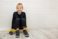 tired smiling cute blond boy sitting on a skateboard after training against a white wall Royalty Free Stock Photo