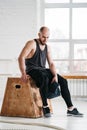 Tired sportsman relaxing on wooden box in fitness gym