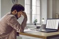 Tired, stressed man sitting at his working desk with a laptop and suffering from a headache Royalty Free Stock Photo