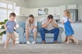 Tired and stressed parents suffering from a headache while adhd kids run around the living room. Noisy naughty siblings