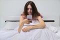 Tired teenager girl sitting at home in bed looking at mobile phone Royalty Free Stock Photo