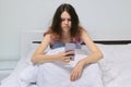 Tired teenager girl sitting at home in bed looking at mobile phone Royalty Free Stock Photo