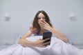 Tired teenager girl sitting at home in bed looking at mobile phone Royalty Free Stock Photo