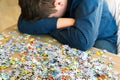 Tired teenager is sitting tilting his head next to puzzles