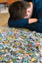 Tired teenager is sitting tilting his head next to puzzles